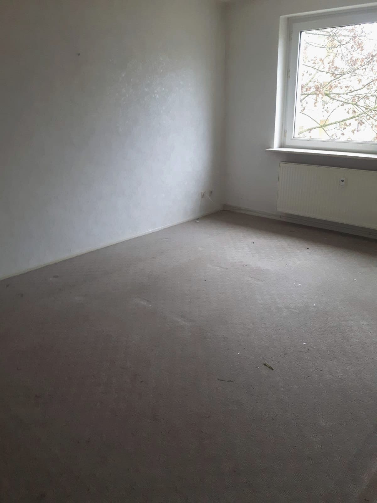 Raum nach Demontage und Räumung: leer, grauer Teppichboden, Fenster