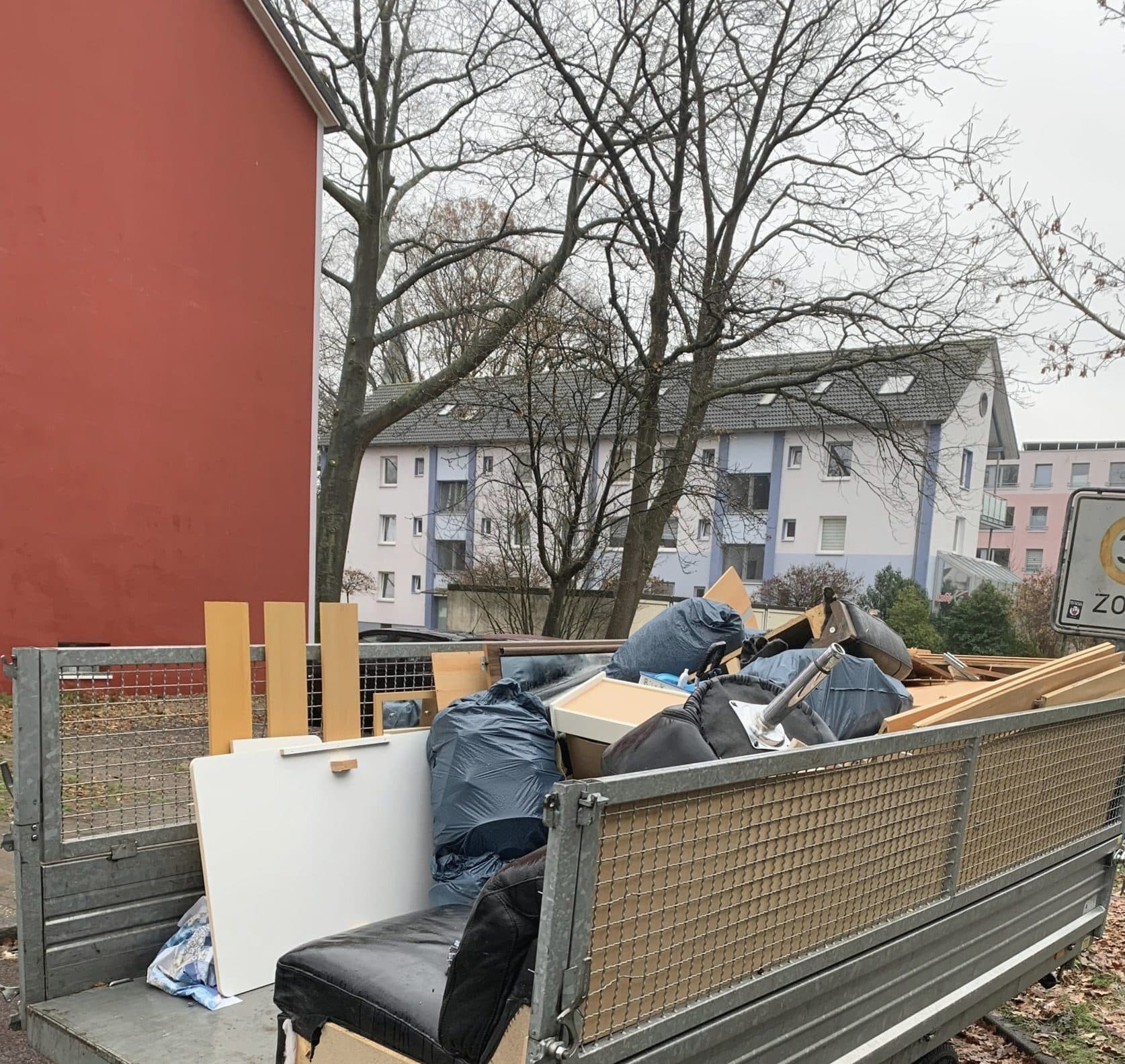 Beladener Anhänger mit Möbelteilen, Brettern und Säcken vor einem Haus